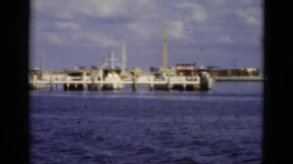 1975 Florida 8mm frame showing moored boats, a pier, pilings, and waterfront structures from a boat on the water.