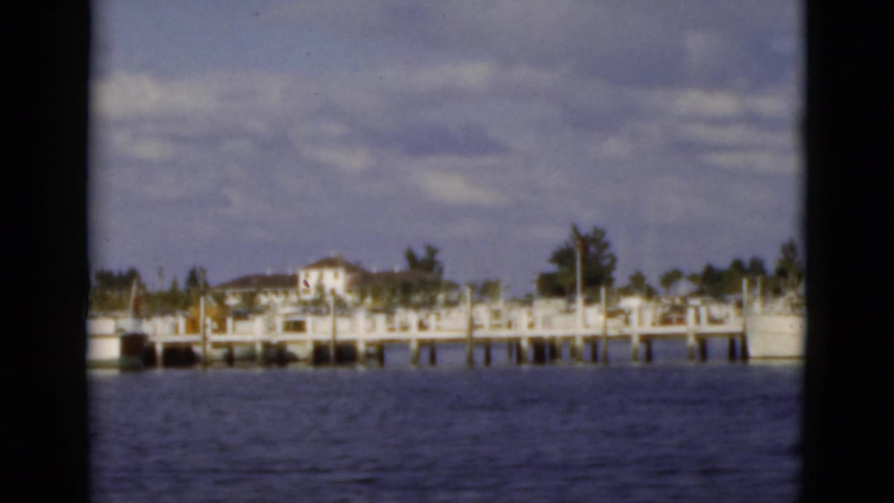 Waterfront houses and docks seen across calm water through dark window framing.