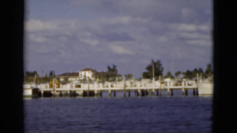 1975 Florida home-movie view of waterfront houses and docks across calm water, framed by dark window edges.