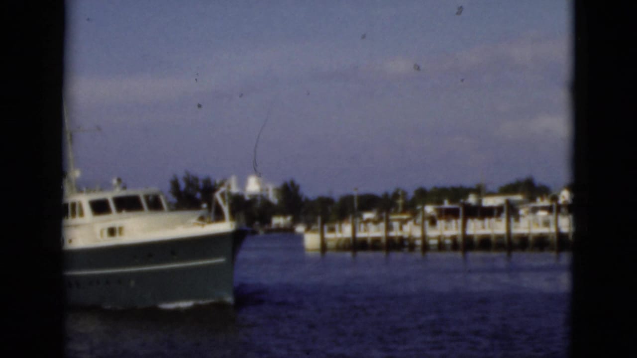 A large white and blue motor yacht passes a dockside residential waterfront in 1975 Florida footage.