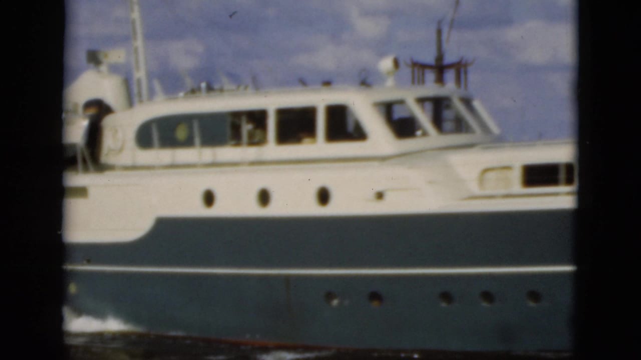1975 Florida 8mm frame showing a white and blue motor yacht in side profile, with cabin windows and portholes visible above the waterline.