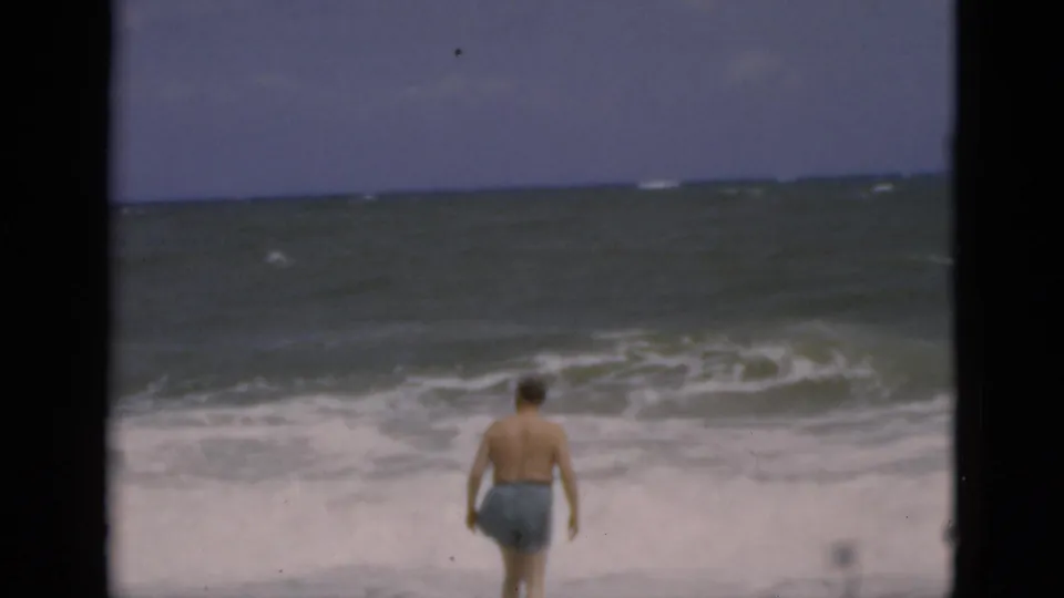The Florida beach footage shows the man from behind in blue swim trunks as he approaches the rough surf and foamy shoreline.
