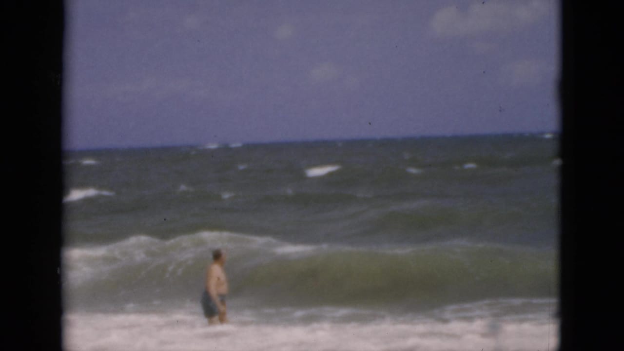 Man wades waist-deep in ocean water as a large wave rises in front of him.