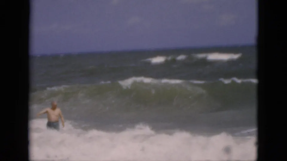 The man appears low in the frame, partly hidden by white surf as rough water rolls toward shore.