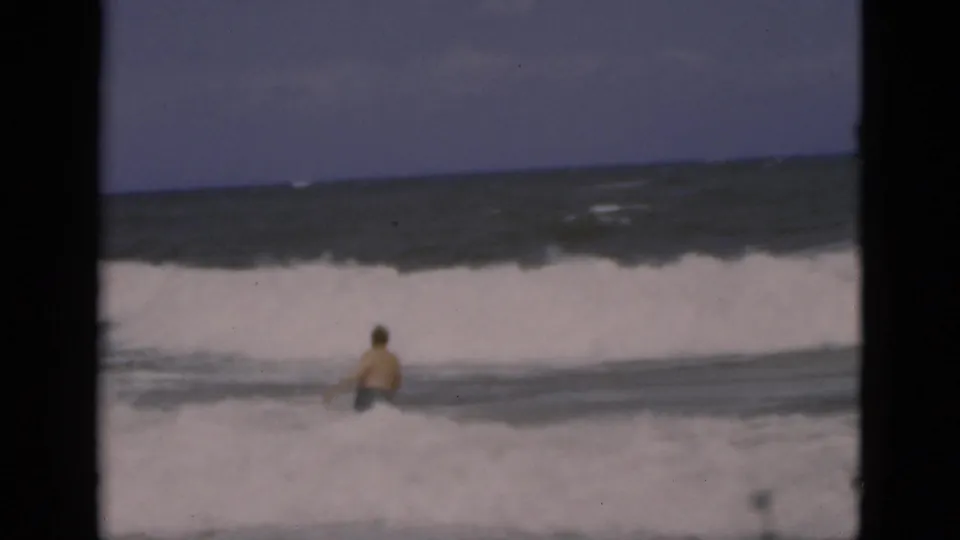 1975 Florida 8mm frame showing the bather from behind in shallow surf as a broad wave breaks across the beach.