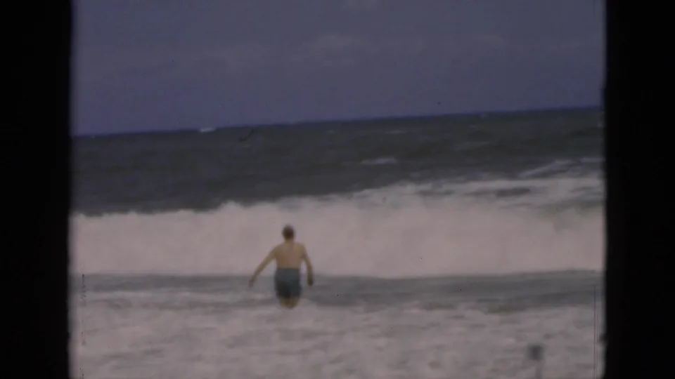 1975 Florida beach frame showing the male bather returning through foamy shallow water, with waves rolling behind him.