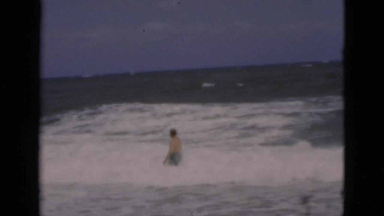 Man stands farther out in foamy ocean water with waves rolling toward shore.
