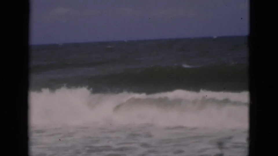 A large white wave breaks across the Florida shoreline scene, filling the 8mm frame with surf, dark water, and a muted sky.