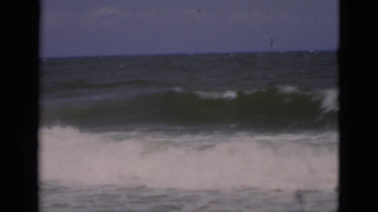 Breaking ocean waves seen through dark 8mm frame borders.