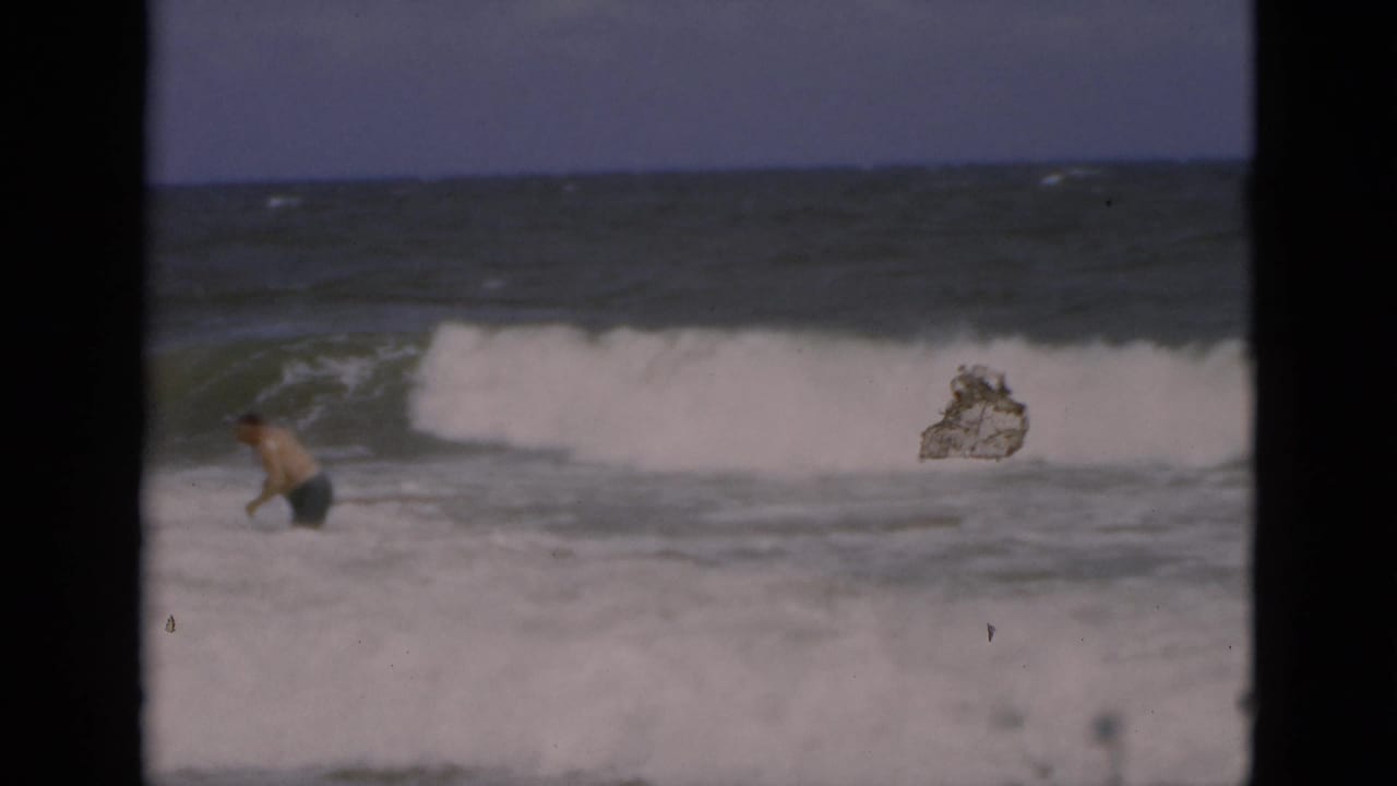 A man wades in the Florida surf as a wave breaks behind him, with a small floating object visible nearby.