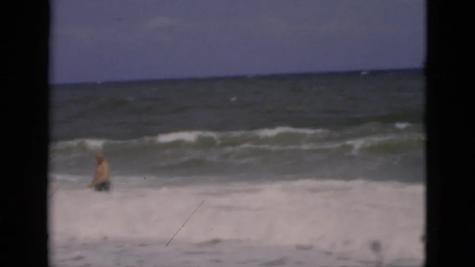 A man remains in the rough Florida surf as white water crosses the foreground and dark frame bars divide the 8mm view.