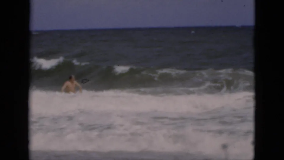The adult swimmer appears farther offshore as a dark green wave rises and white water breaks around him.