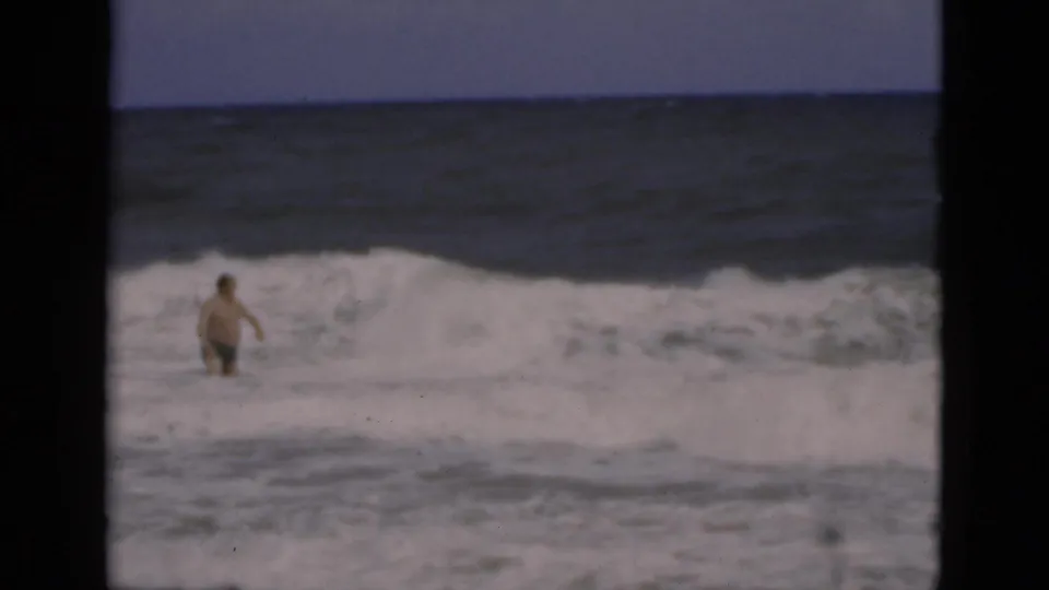 The shirtless man moves through dense white water in the Florida surf, with the open ocean and film borders visible.