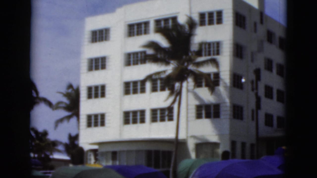 White beachside building with palm tree behind colorful tents and umbrellas.