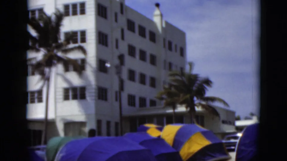 1975 Florida beach scene showing tents and an umbrella below a white resort-like building and palm trees.