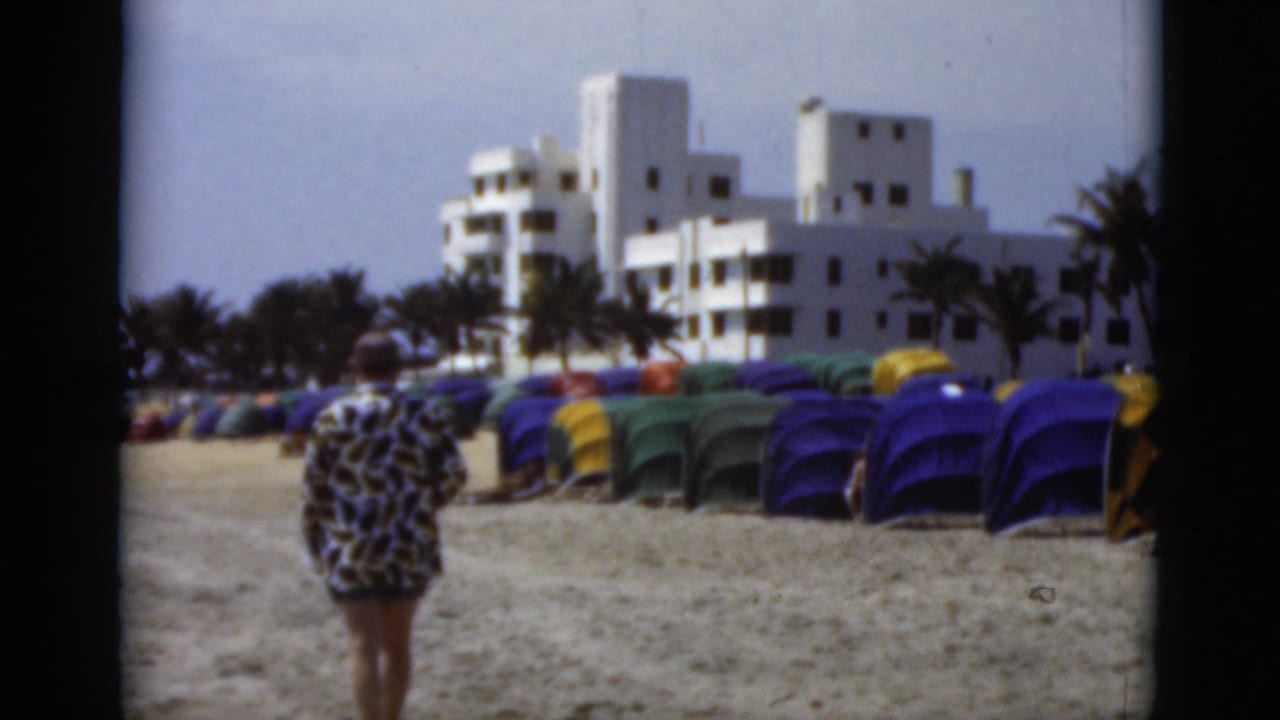 Man seen from behind walking on a sandy beach near rows of colorful tents.