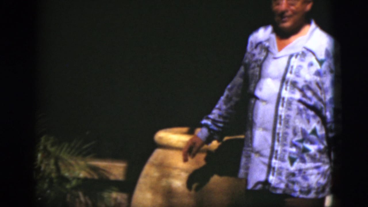 Man in patterned shirt stands beside a large ceramic pot on a dark stage.