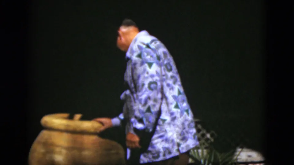 In the final frame, the man bends toward the large ceramic pot, appearing to look inside during the stage-like moment.