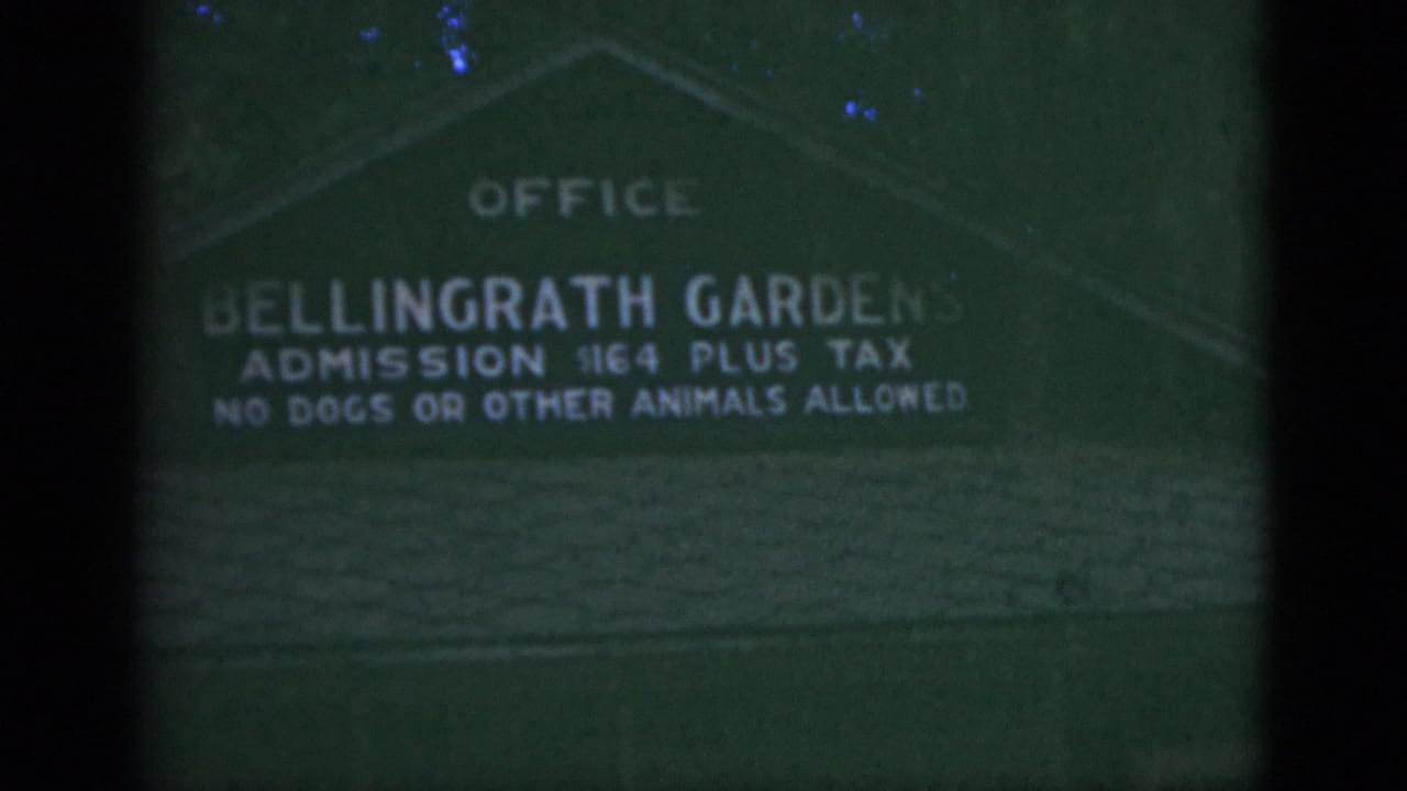 Green Bellingrath Gardens office sign seen through a dark film frame edge.