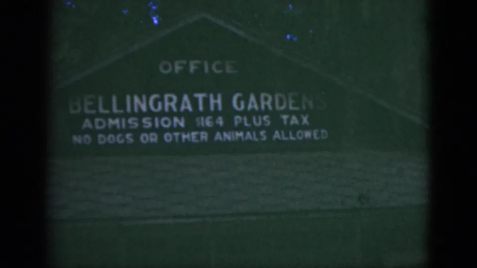1975 8mm frame of a green Bellingrath Gardens office sign with admission text, partly obscured by dark frame borders.