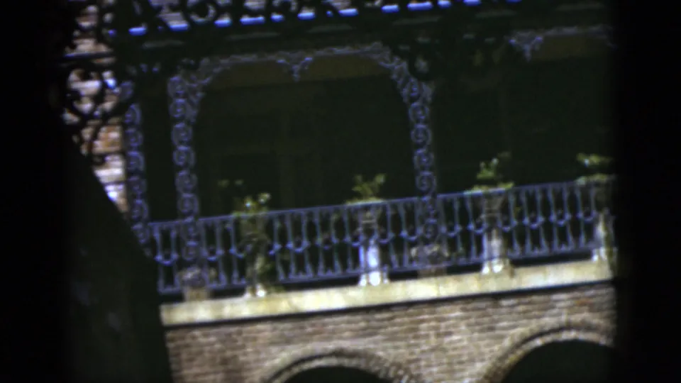 1975 Florida 8mm frame showing an older brick house exterior with arched openings, decorative balcony rail, and dark foreground obstruction.