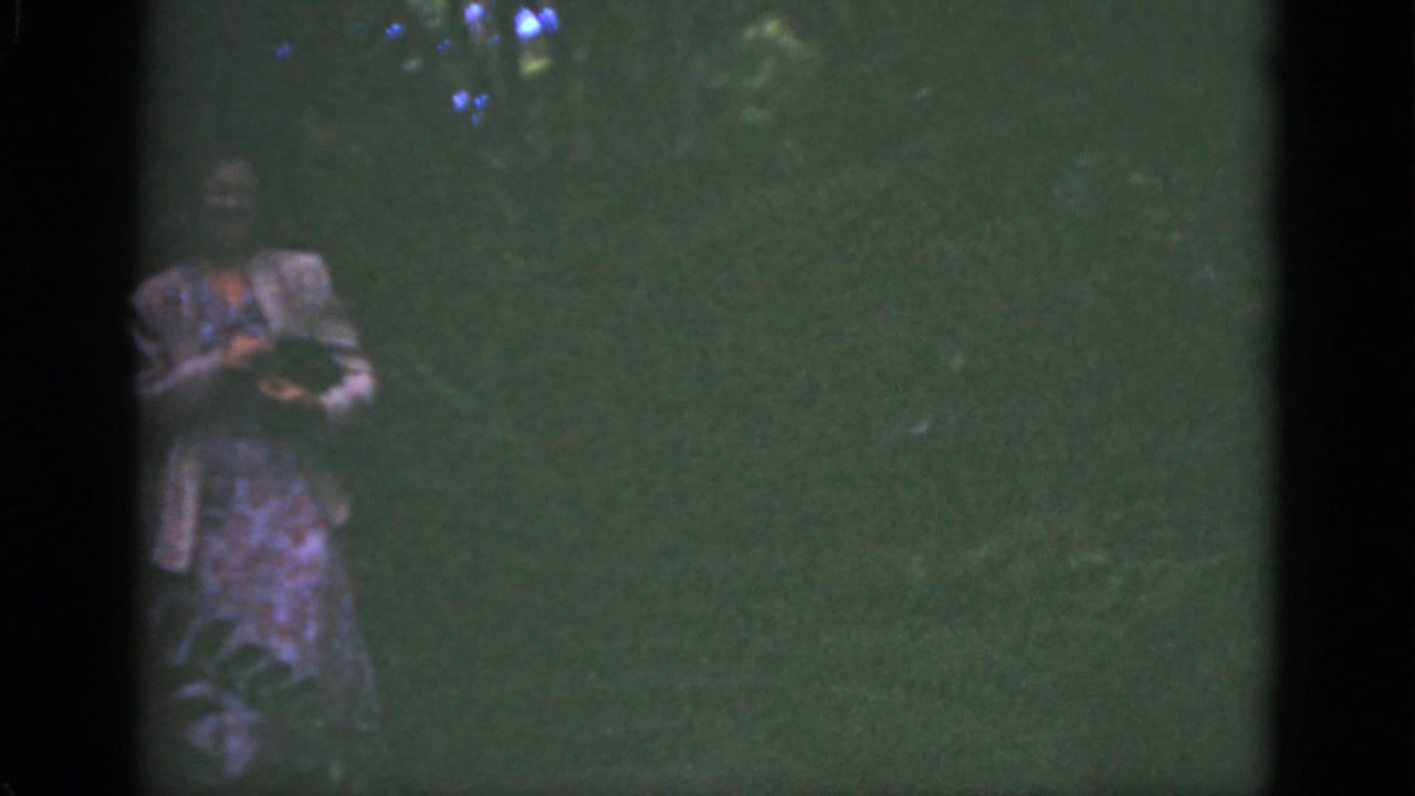 In 1951 Florida home-movie footage, a woman in a patterned dress and light jacket appears in shaded foliage holding a small animal.