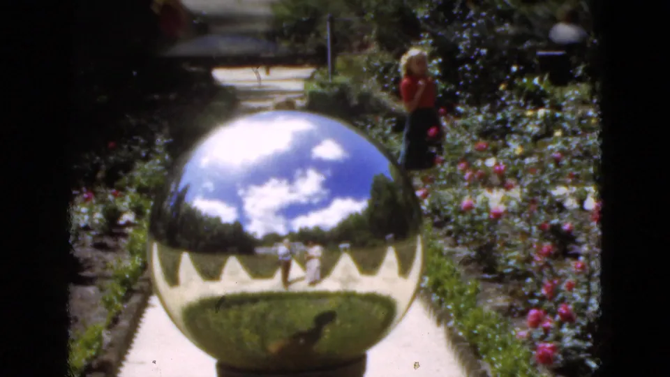 1951 Florida garden view with a chrome-like sphere reflecting sky and walkway, with an adult woman visible near rose beds.