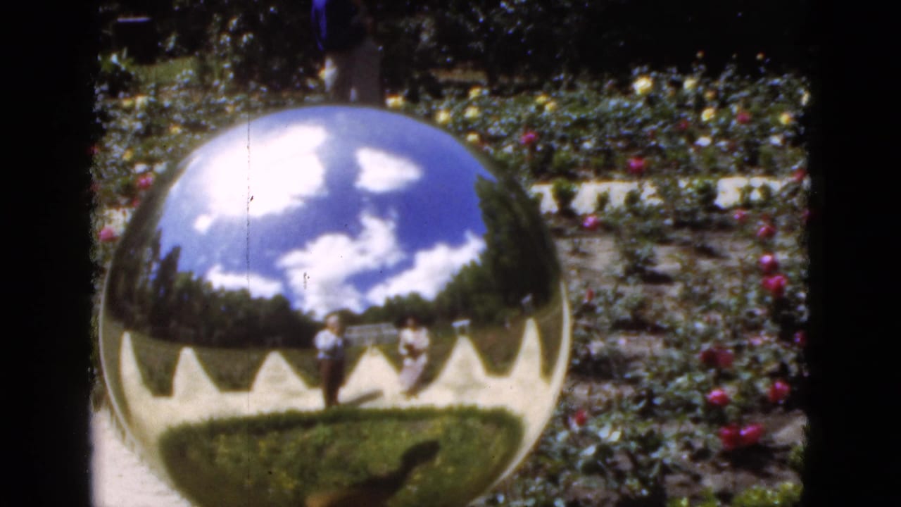 1951 Florida garden footage showing a shiny metallic sphere reflecting blue sky, white clouds, paths, flower beds, and nearby visitors.