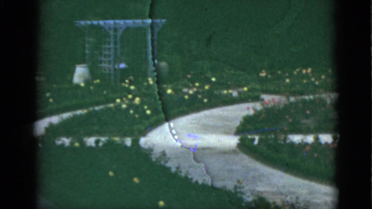 Curving pale path through green lawn with flowers and a metal arbor in the background.