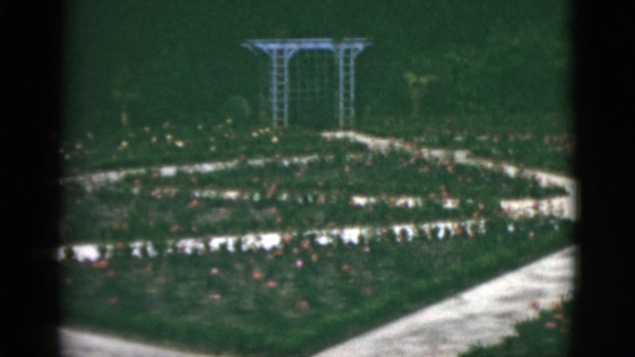 Rose garden paths curve through flower beds toward a white trellis.