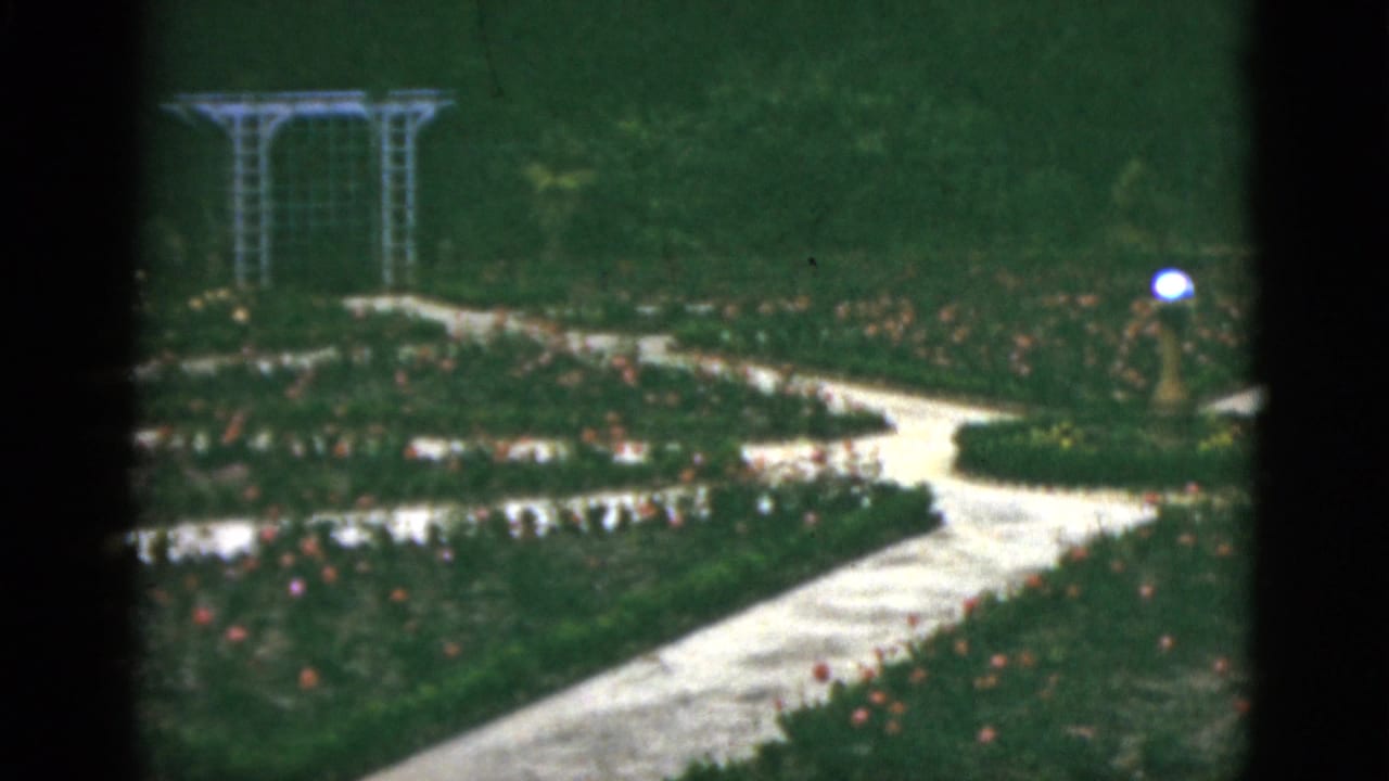 Curving garden path, rose beds, white trellis, and globe lamp.