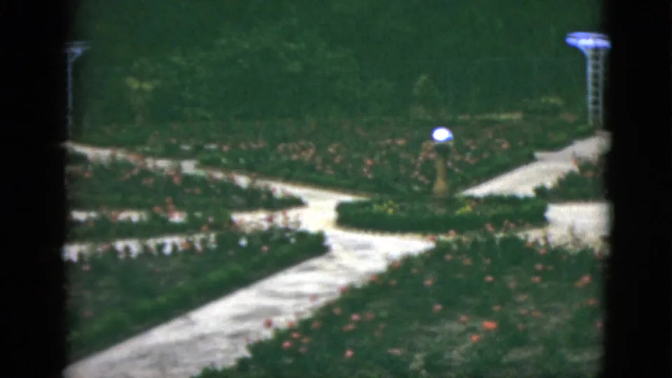 1951 Florida 8mm frame showing intersecting garden paths, rose beds, a globe-topped lamp, and part of a white trellis at the right edge.