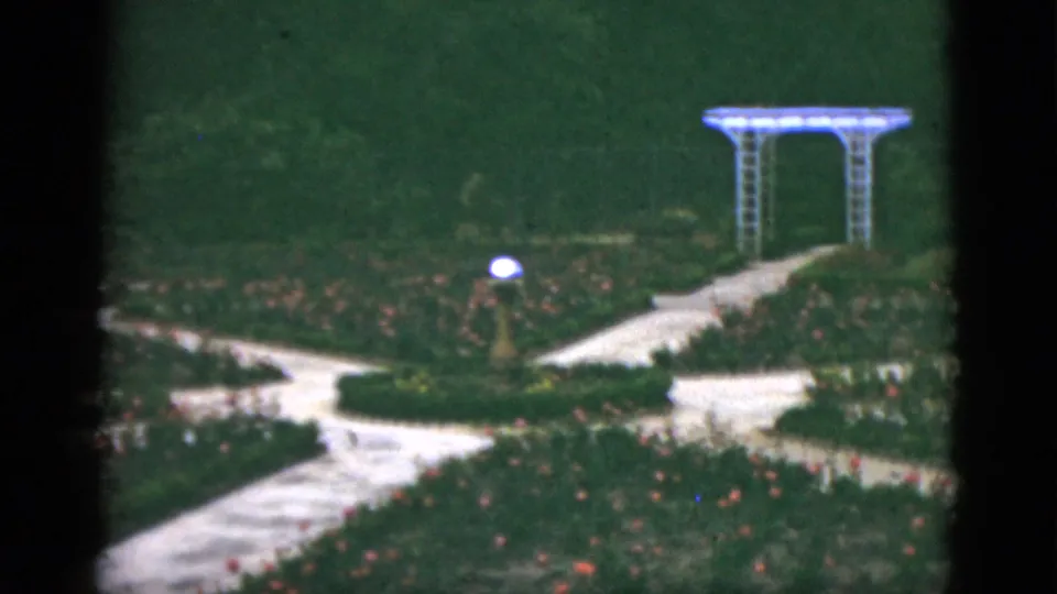 1951 Florida garden frame with a winding pale path, rose beds, trimmed greenery, a globe lamp, and a white trellis in the background.