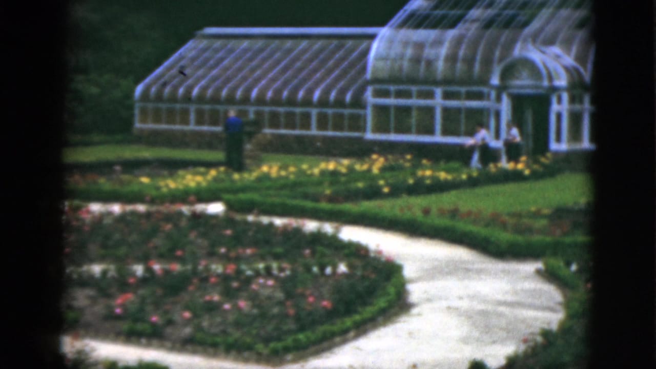 Glass greenhouse and formal garden paths with several visitors near the entrance.