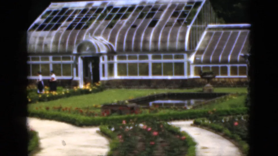 1951 Florida garden view with the greenhouse, visitors at left, planted beds, a small pond or pool, and curving paths.