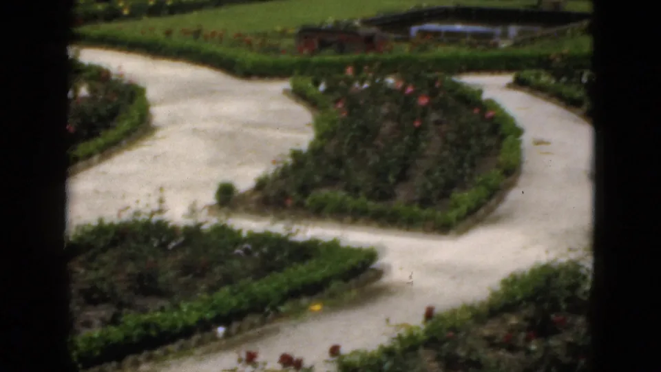 1951 Florida garden frame with sweeping concrete walkways around clipped planting beds, rose bushes, lawn, and a small pond in the distance.