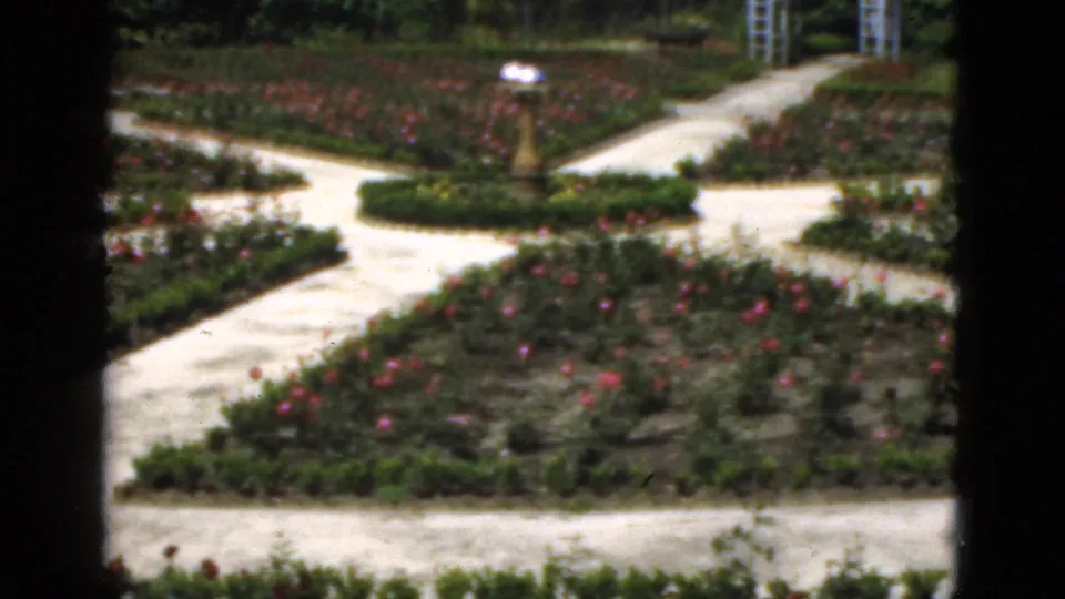 1951 Florida garden frame with crossing pale paths, a central lamp post, rose beds, and distant visitors in soft focus.