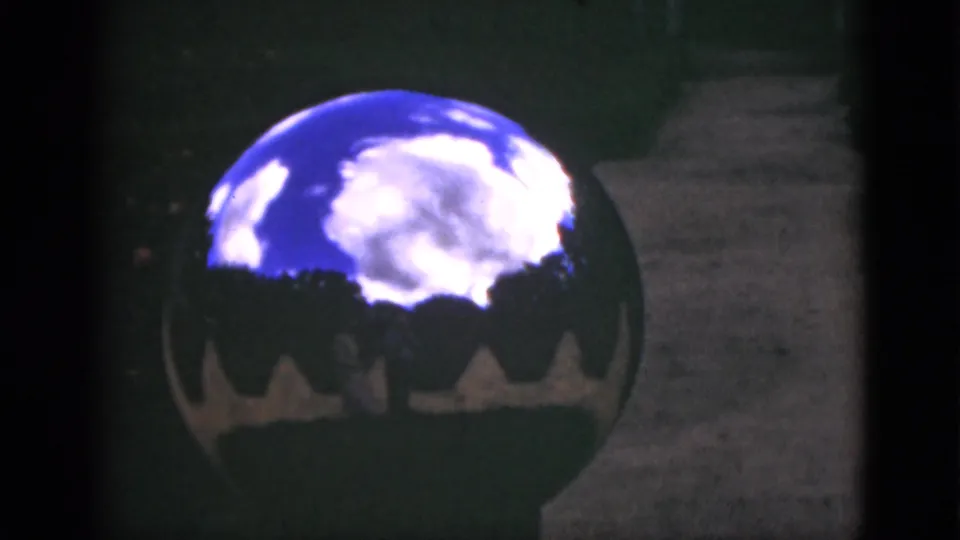 Close 1951 Florida home-movie view of a mirrored garden globe reflecting clouds and trees, with lawn and a walkway behind it.
