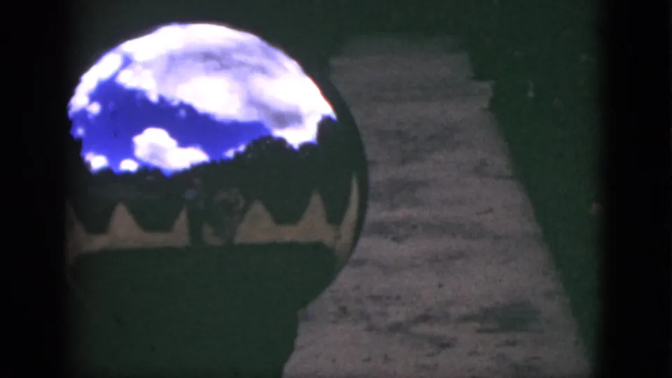 1951 Florida frame of the garden globe near a stone path, with bright clouds and dark tree shapes reflected across the curved surface.