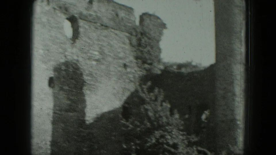1951 West Germany 8mm frame showing a crumbling castle wall with dark arched openings and overgrown plants.