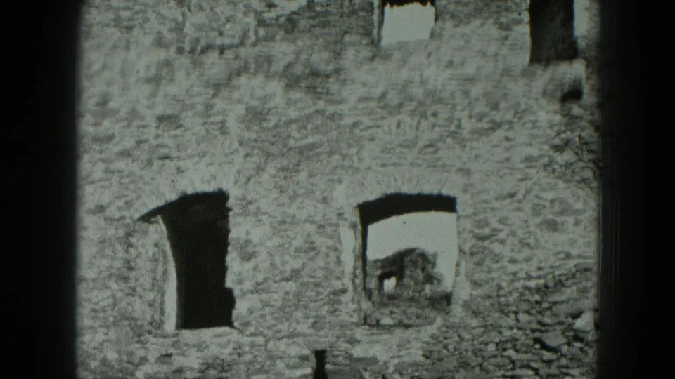 1951 West Germany 8mm frame of a weathered stone building facade with empty window openings and uneven masonry.