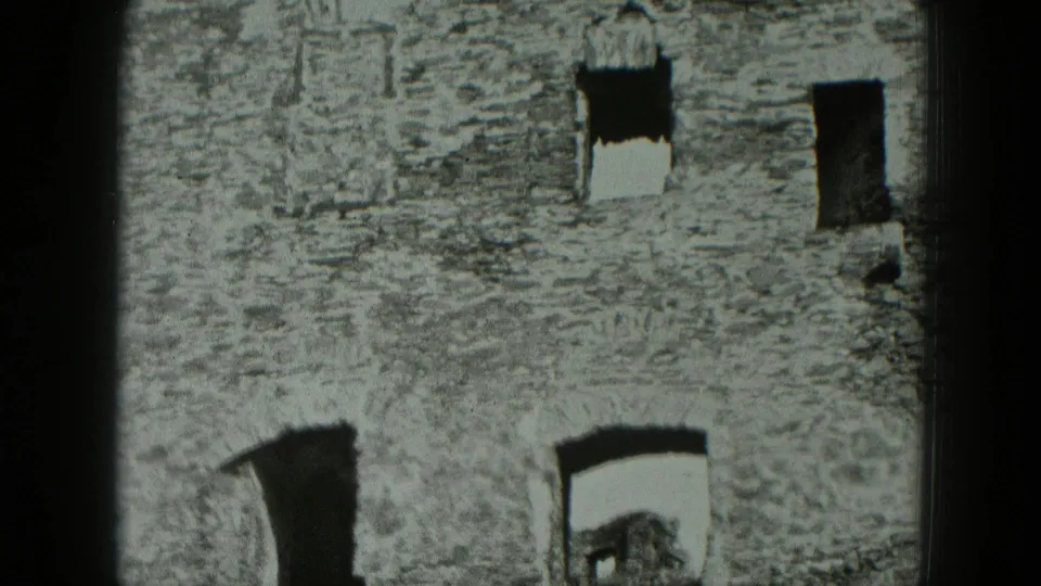 1951 West Germany 8mm frame showing a close section of crumbling stone wall with empty window openings and rough masonry texture.