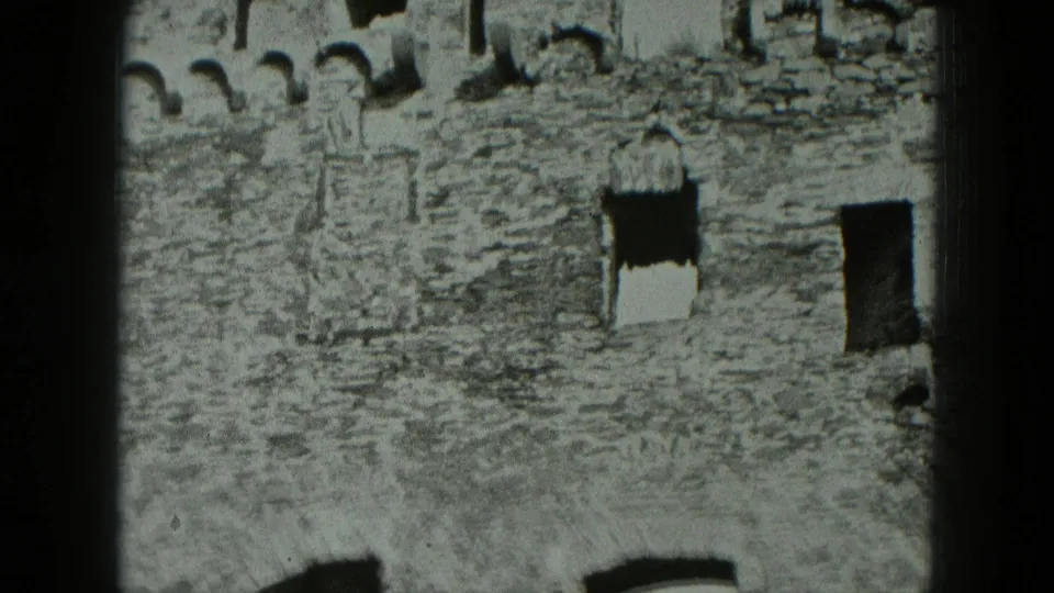 1951 West Germany 8mm frame of a stone building wall with multiple empty openings, rough texture, and visible film framing.