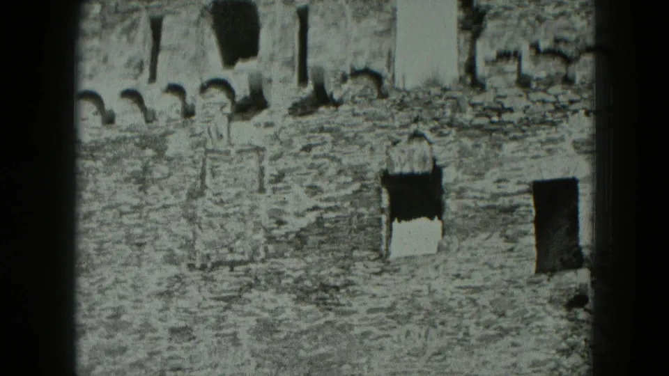 1951 Germany 8mm frame showing a high stone castle ruin wall with arched openings, dark windows, and rough masonry.