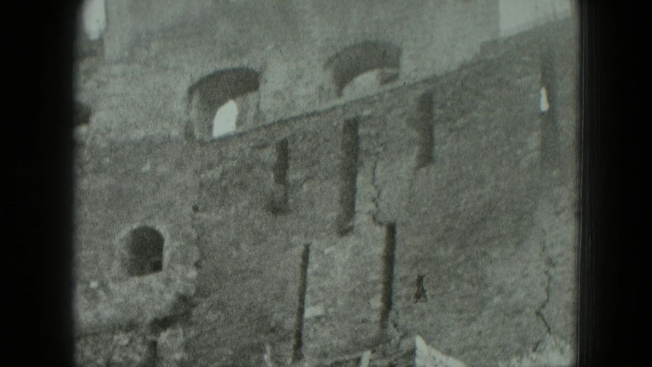 1951 Germany 8mm frame of a damaged multi-story brick facade with arched openings and fractured wall surfaces.