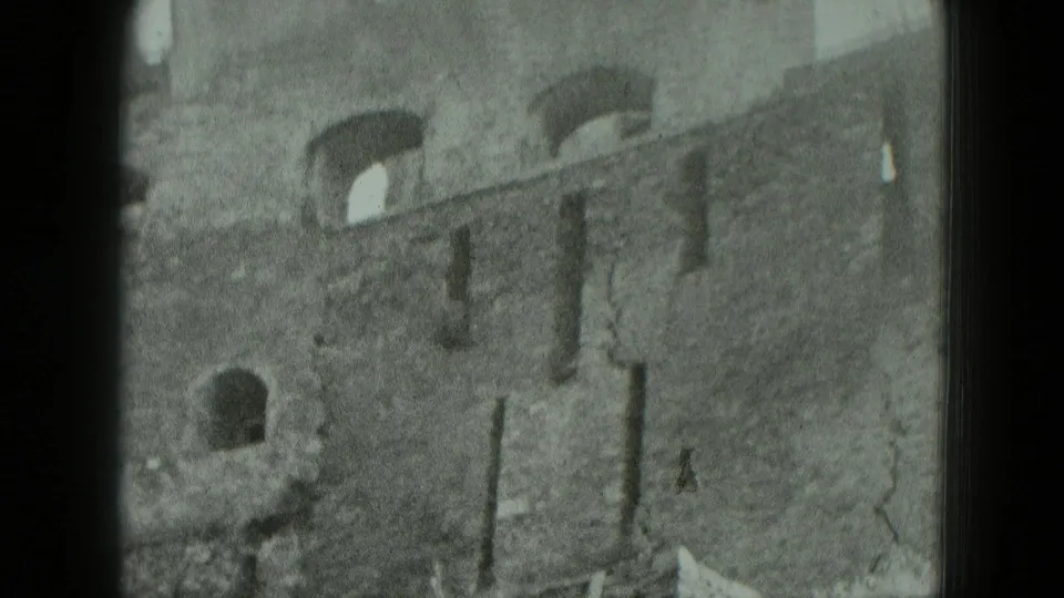 1951 Germany 8mm frame of a damaged multi-story brick facade with arched openings and fractured wall surfaces.