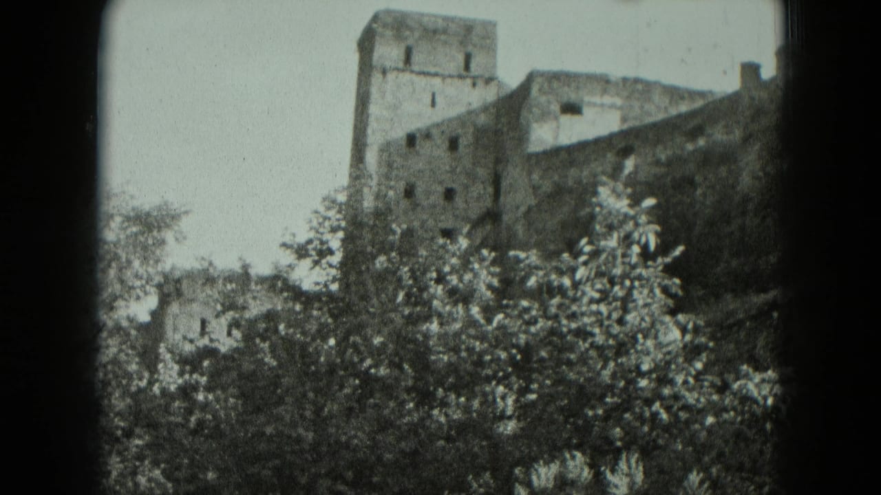 1951 Germany 8mm frame of a ruined stone structure with a square tower, small windows, and leafy trees in the foreground.