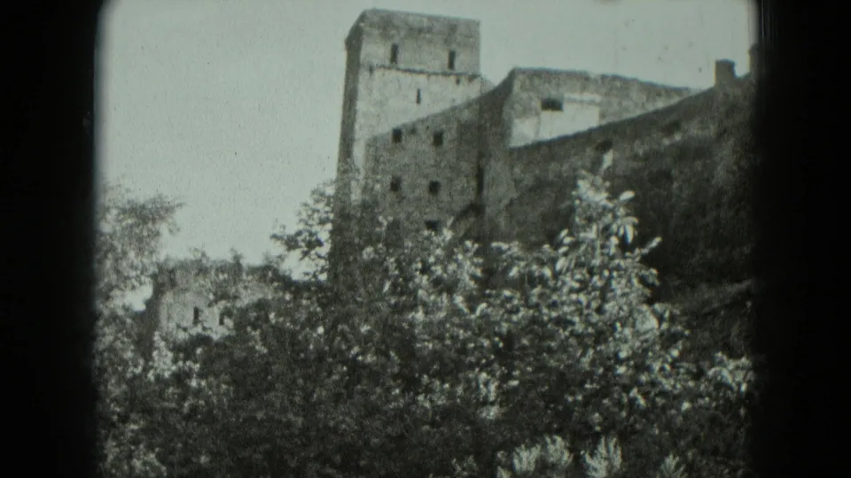 1951 Germany 8mm frame of a ruined stone structure with a square tower, small windows, and leafy trees in the foreground.