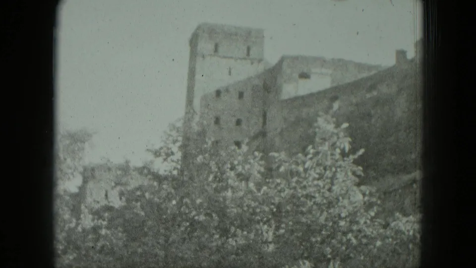 1951 Germany 8mm frame with soft exposure showing a ruined tower and wall line behind leafy vegetation.