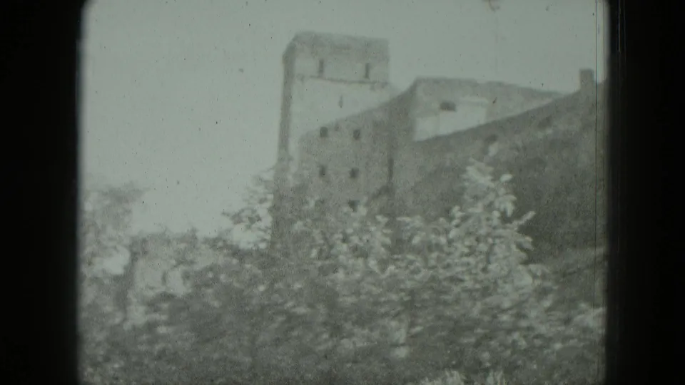 A hilltop castle or fortified building in Germany, supplied as 1951 footage, appears beyond leafy trees in soft 8mm focus.